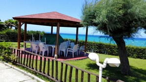 A gazebo with a red roof, surrounded by white plastic chairs and a table, overlooking a clear blue sea.