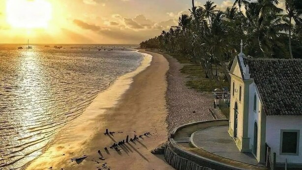 A beach with a small building, palm trees, and boats. - Pousada Cambará (Tamandaré)