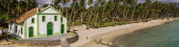 Een wit gebouw met groene details, een strand en palmbomen.