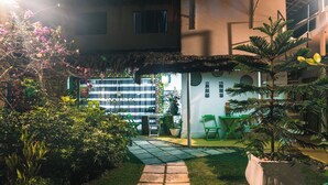 A well-maintained garden with a pathway leading to a seating area, surrounded by lush greenery and a thatched roof structure. - Pousada Cambará (Tamandaré)