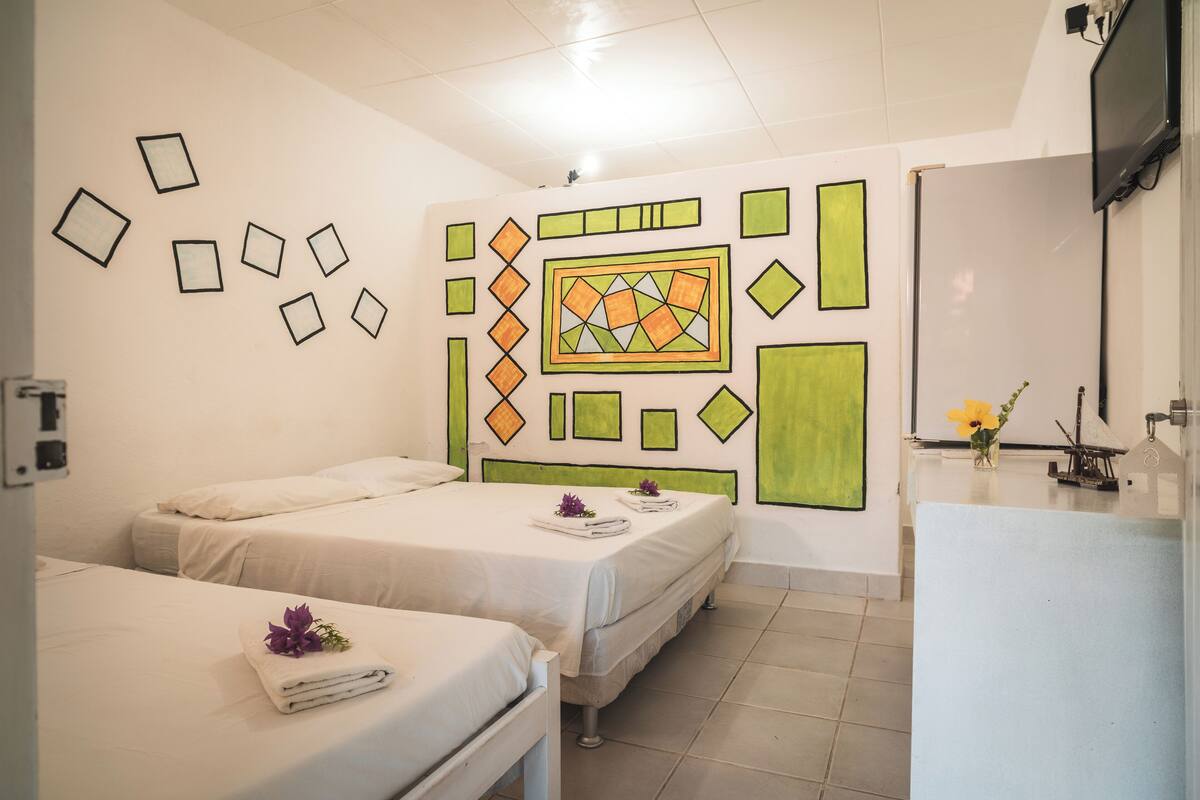 Une chambre d’hôtel avec deux lits, une salle de bain et un mur orné de motifs géométriques.
