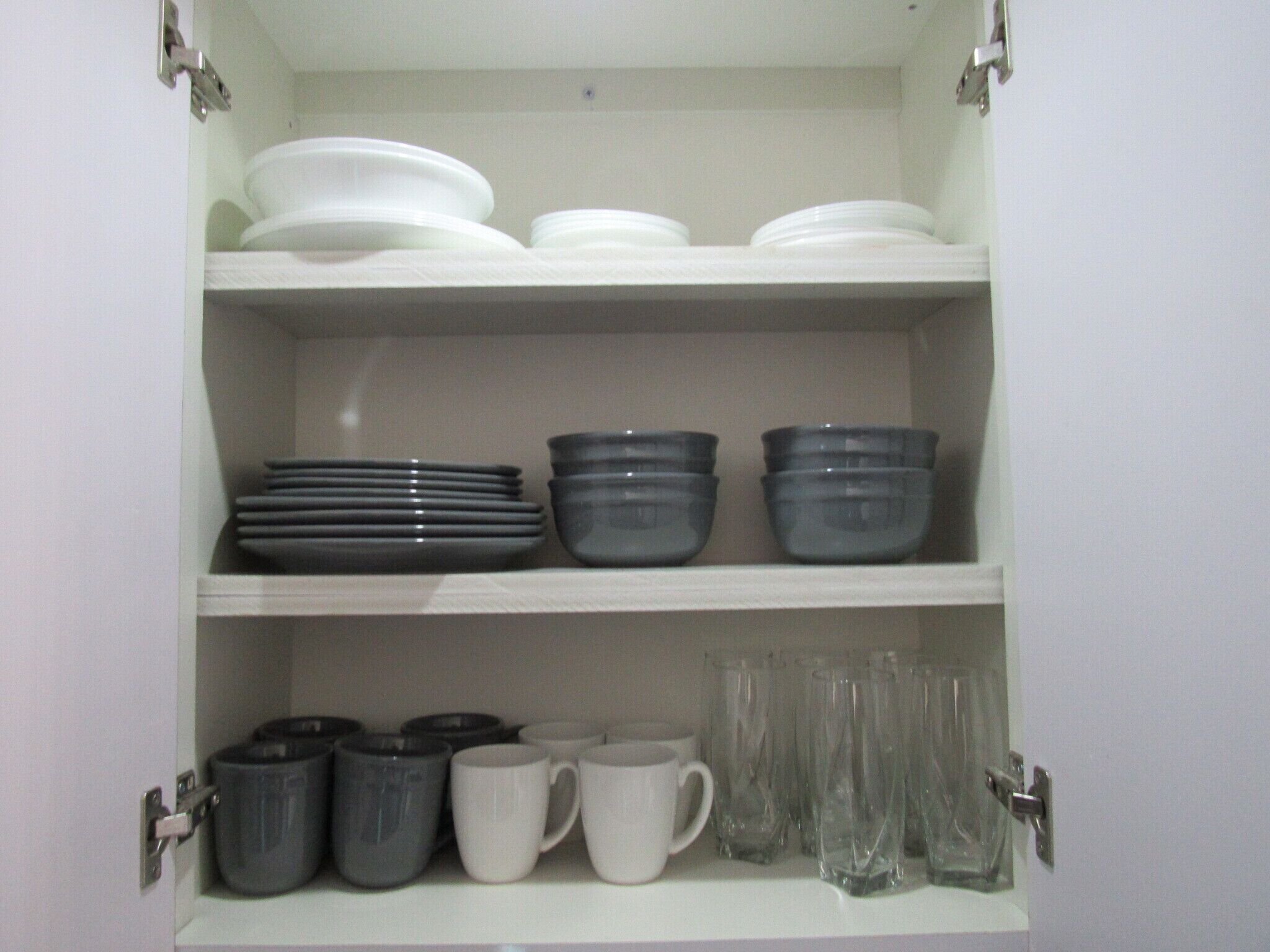 A cabinet with shelves containing plates, bowls, mugs, and glasses.