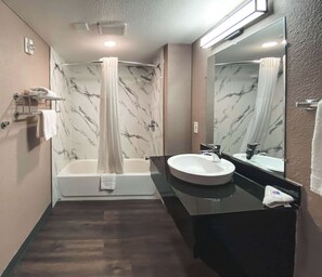 A modern bathroom with a marble shower wall, a bathtub, a round sink, and a large mirror. - Studio 6 West Sacramento, CA (West Sacramento)