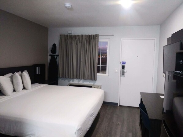 Une chambre d’hôtel avec un grand lit, un bureau, une télévision, une fenêtre avec des rideaux et une porte.