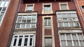 Un edificio de varios pisos con fachadas en tonos rojo y beige, grandes ventanas y una tienda visible con señalización.