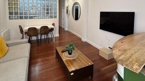 Una sala de estar moderna con comedor, un ventilador de techo, un televisor montado en la pared y un ventanal con vistas.