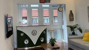 Una sala de estar con una furgoneta VW clásica, un ventilador de techo, un reloj y una planta en maceta.