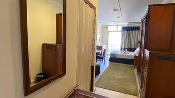A hotel room with a wooden bench, a large mirror, a bed, a desk, and a small rug.