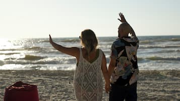 Dos personas caminando sobre una playa arenosa con una bolsa roja y un cielo despejado.
