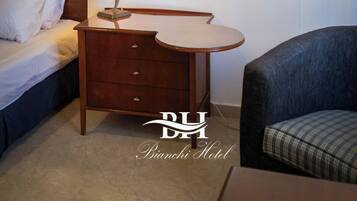 A hotel room with a bed, a wooden nightstand with a lamp, a mirror, and a chair.