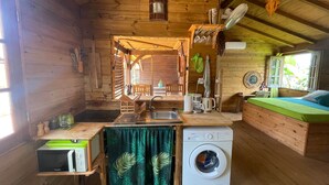 Een knus houten huisje met een kitchenette, een wasmachine en een bed.
