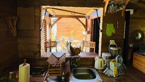 Een eenvoudige houten keuken in een blokhut, met een houten tafel, stoelen, een spoelbak en verschillende keukengerei.