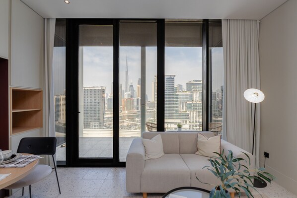 A modern living room with a large window, a sofa, a dining table, and a lamp.