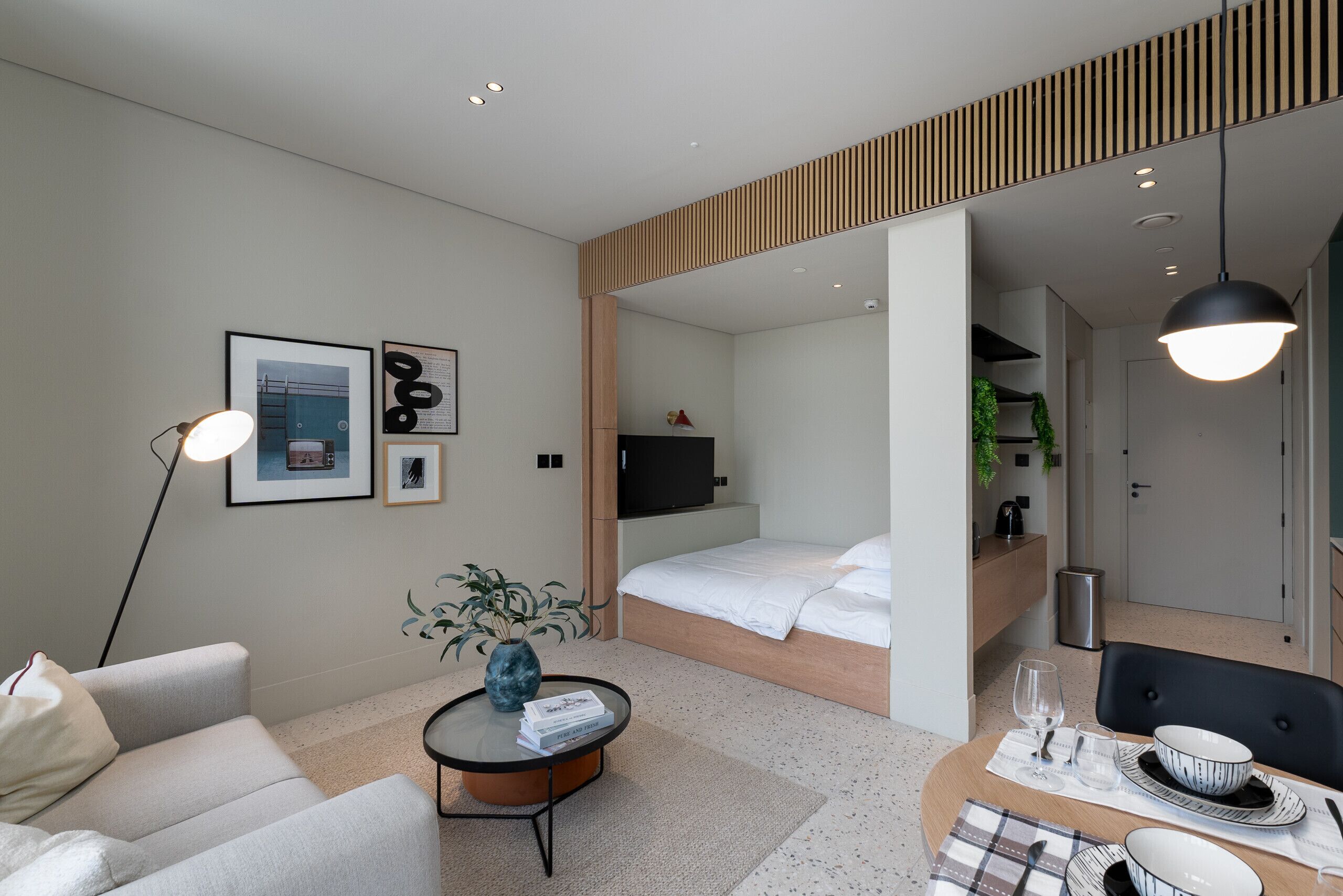 A modern hotel room with a bed, a sitting area with a sofa and coffee table, and a dining area with a table set for two.