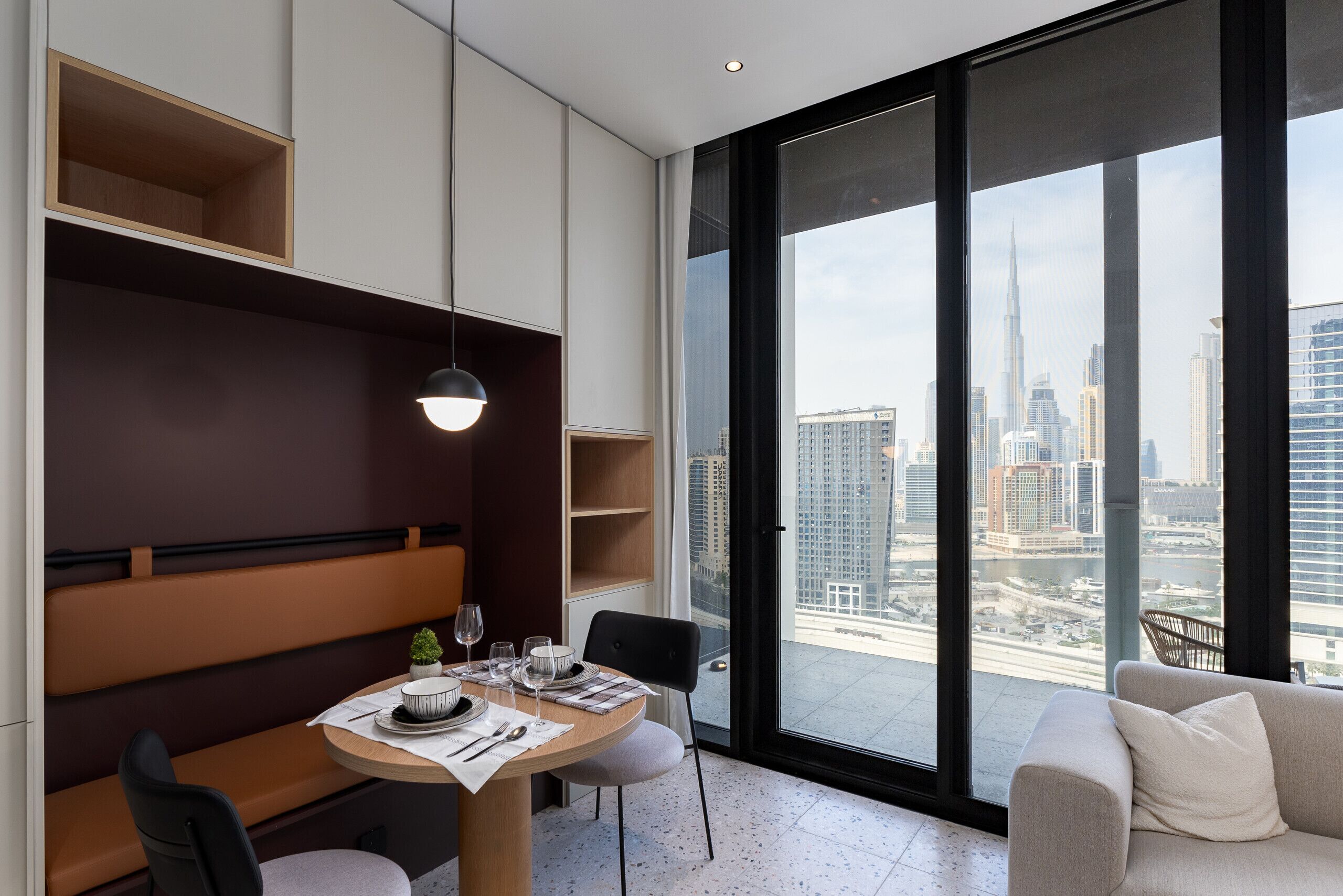 Un espace de salle à manger moderne avec une table ronde, des chaises et une vue sur le paysage urbain grâce à de grandes fenêtres.
