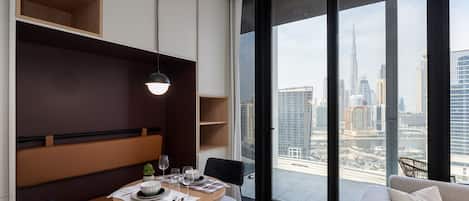 A modern dining area with a round table, chairs, and a view of a cityscape through large windows.