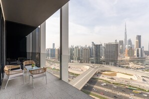 Un balcón con mobiliario de mimbre y vistas a un paisaje urbano que incluye un rascacielos destacado.