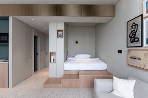 Un dormitorio moderno con cama, asientos integrados, un pequeño escritorio y una obra de arte enmarcada en la pared.
