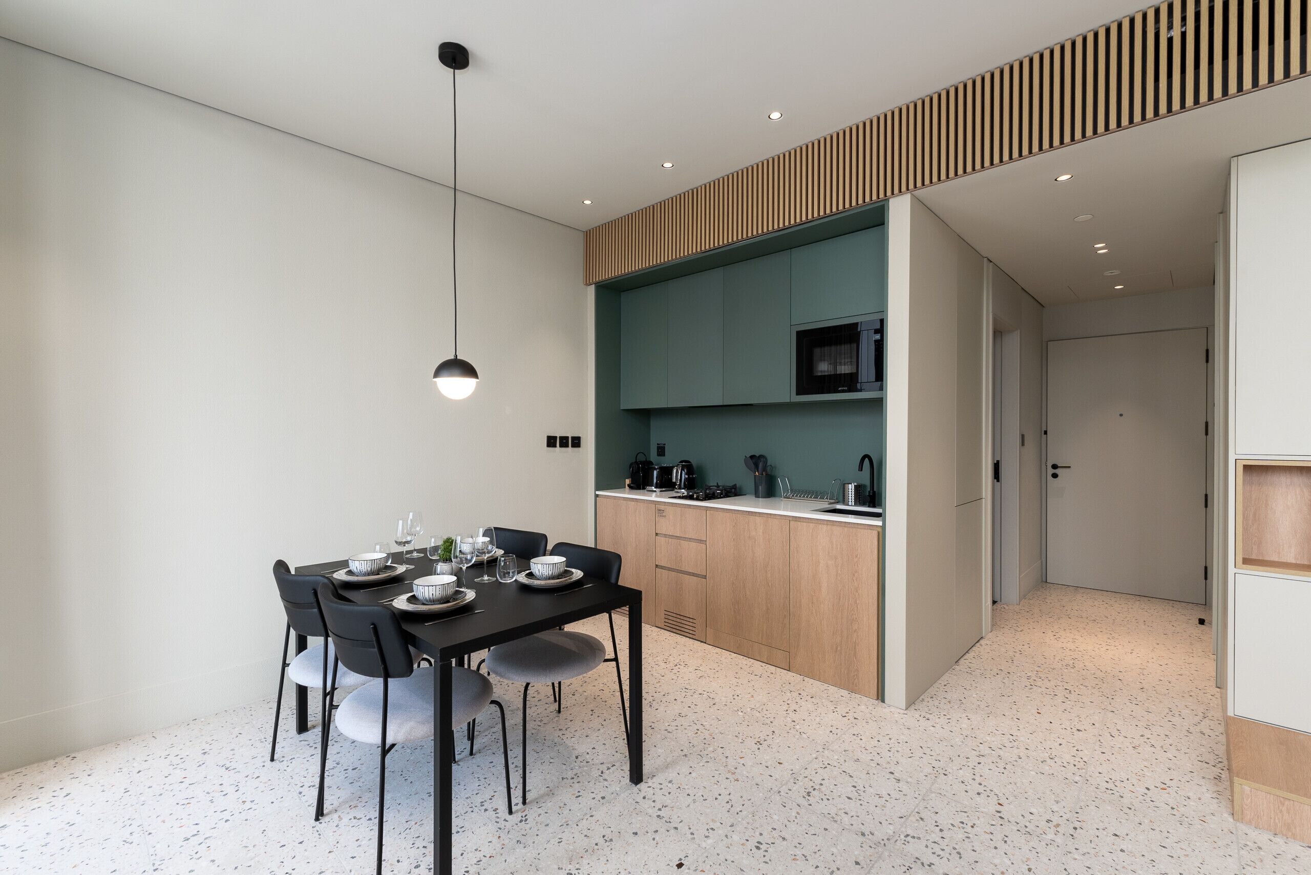 Una cucina moderna con zona pranzo, caratterizzata da un tavolo da pranzo nero, sedie grigie e una lampada a sospensione.
