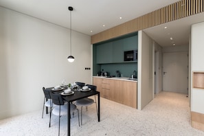 A modern kitchen with a dining area, featuring a black dining table, grey chairs, and a pendant light.