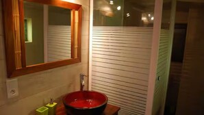 Un bagno con un mobile vanitario in legno, un grande specchio, un lavandino rosso e un dispenser per sapone verde.