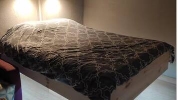 Uma cama com colcha estampada, cabeceira de madeira e duas luminárias fixadas na parede.