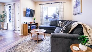 Una sala de estar moderna con un sofá gris, una mesa redonda de centro y un ventanal con cortinas.