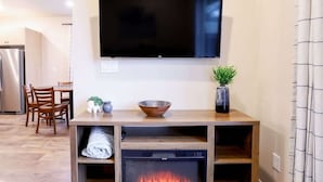 Una sala de estar con televisor de pantalla plana montado en la pared, una unidad de entretenimiento de madera con chimenea y una zona de comedor con sillas y una mesa.