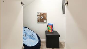 A small, enclosed bathroom with a blue pet bed, a wall-mounted toilet paper holder, and a box of 'Dinosaur' themed toilet paper.
