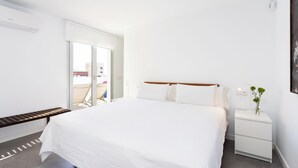 Habitació d'hotel moderna amb un llit gran, una tauleta de nit amb una làmpada i vista per una porta corredissa a una zona exterior.