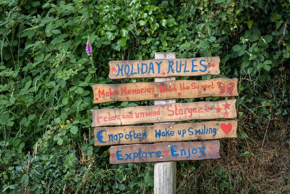 A wooden sign with multiple wooden boards, each with handwritten text and symbols, set against a backdrop of green foliage.