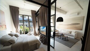 Une chambre moderne avec un grand lit, un canapé, une table basse et une vue sur la ville grâce à de grandes fenêtres.