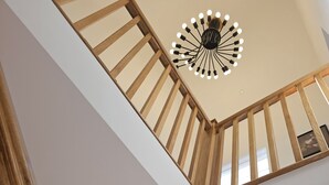 Un intérieur moderne avec un escalier en bois, un luminaire suspendu au plafond et des spots encastrés.