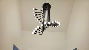 Un couloir avec une porte en bois, un escalier avec une rampe en bois et un luminaire moderne doté de plusieurs ampoules.