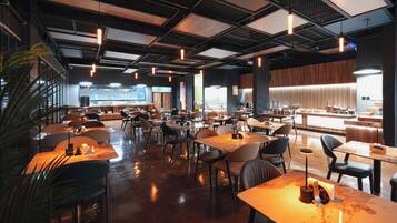 A spacious restaurant with multiple tables and chairs, a bar area, and a large window providing a view of the city.