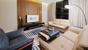 A modern living room with a sofa, armchair, and a coffee table. A flat-screen TV is mounted on the wall, and there is a floor lamp.