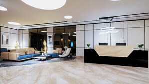 A modern lobby with a reception desk, seating area, and a large mirror.