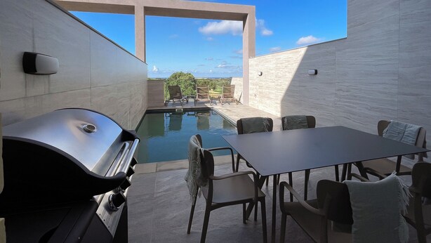Un patio exterior moderno con piscina, zona de parrillada y mobiliario.
