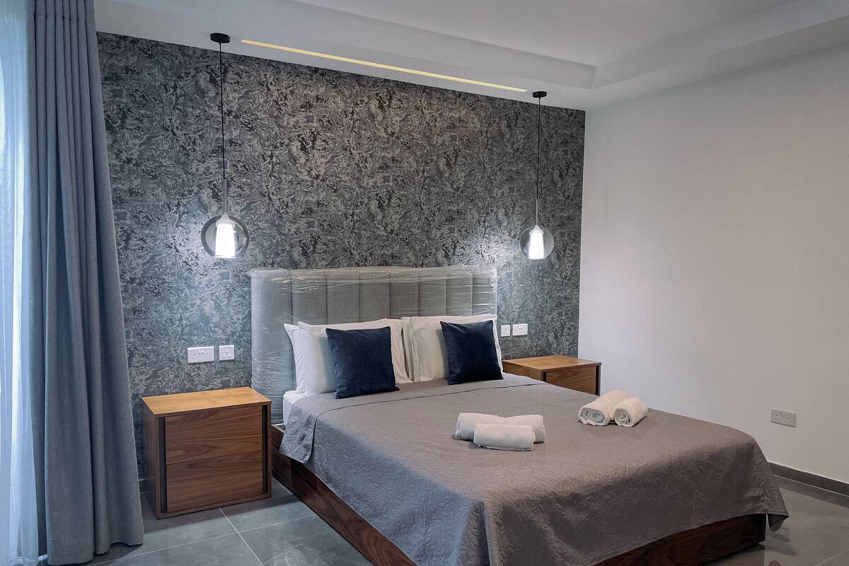 Ein modernes Schlafzimmer mit einem großen Bett, zwei Nachttischen, einer Kopfteil und einer strukturierten Wand.