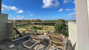 Un balcón con dos sillones de descanso y una mesa, con vistas a un paisaje rural con edificios y vegetación.