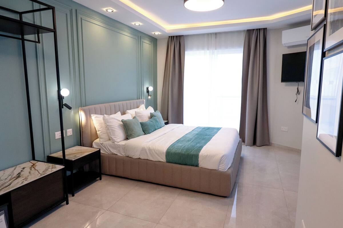 Ein modernes Schlafzimmer mit einem großen Bett, Nachttischen, einem Spiegel und einem an der Wand montierten Fernseher.