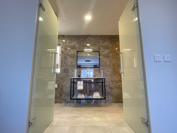 A modern bathroom with a glass partition, marble walls, a sink with a mirror, and a towel rack. - Pietro Boutique Hotel and Residences (Gharb)