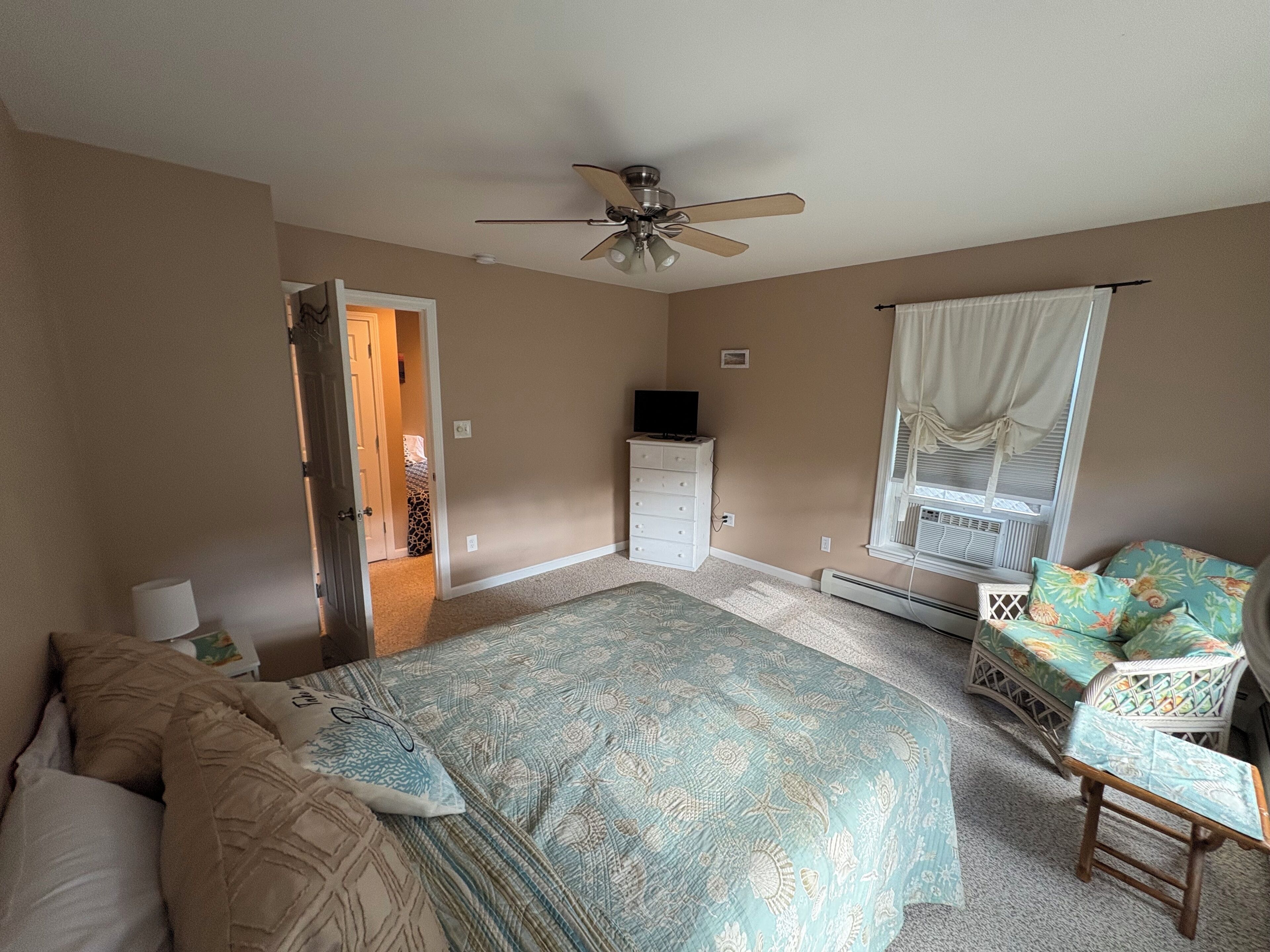 Une chambre à coucher avec un lit, une chaise, un téléviseur et un ventilateur de plafond.