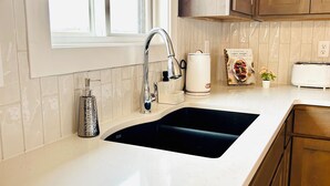 A kitchen with a white countertop, a black sink, wooden cabinets, a window, and a toaster. - New construction, Sunset views  (Lincoln)