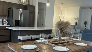 A modern kitchen with a built-in refrigerator, a dining area with a wooden table set for six, and a chandelier above. - New construction, Sunset views  (Lincoln)
