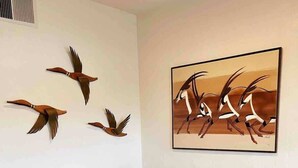 A dining area with a round wooden table, four leather chairs, and a wall-mounted painting of antelopes. - Memories on McKinley | Downtown | Central (Phoenix)