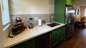 A kitchen with green cabinets, a stainless steel refrigerator, a sink, and a countertop with a blender and a basket.