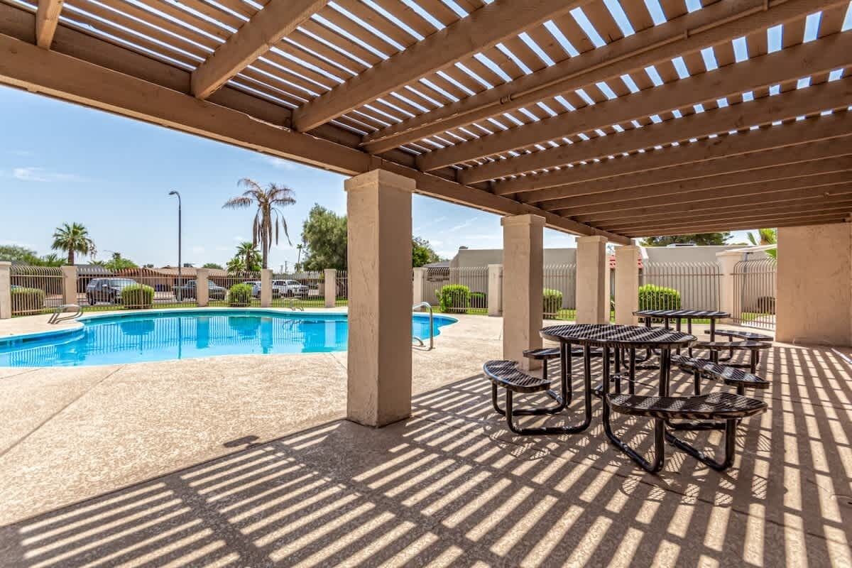 A covered outdoor pool area with picnic tables and lounge chairs.