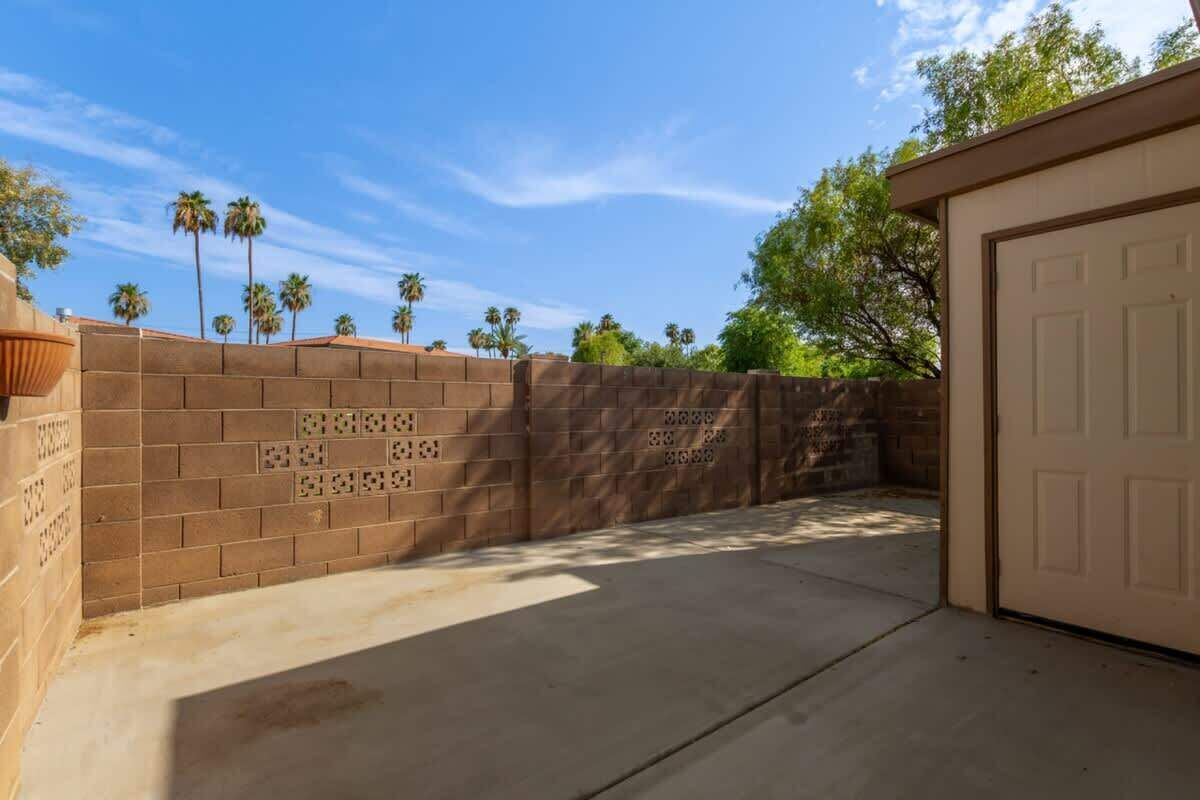 Un muro de ladrillo con una puerta de garaje, un camino de hormigón y palmeras al fondo.