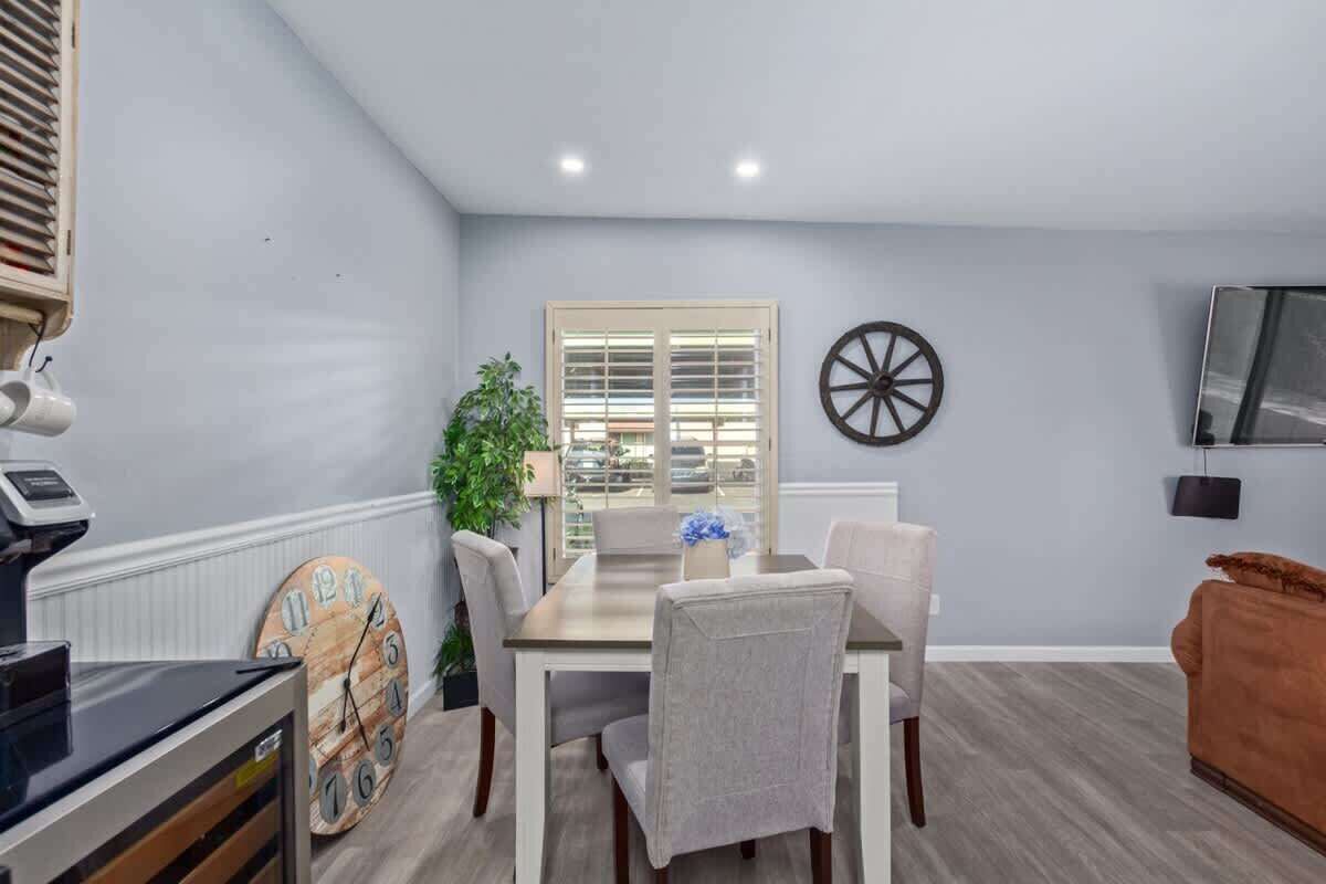 A dining area with a table, chairs, a clock, a plant, and a wall-mounted TV.